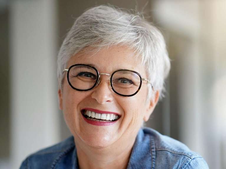 A cheerful woman in glasses and a denim shirt, inviting viewers to explore All-on-4® Implants option