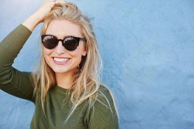 A smiling woman in sunglasses considers Invisalign® with partial dentures.