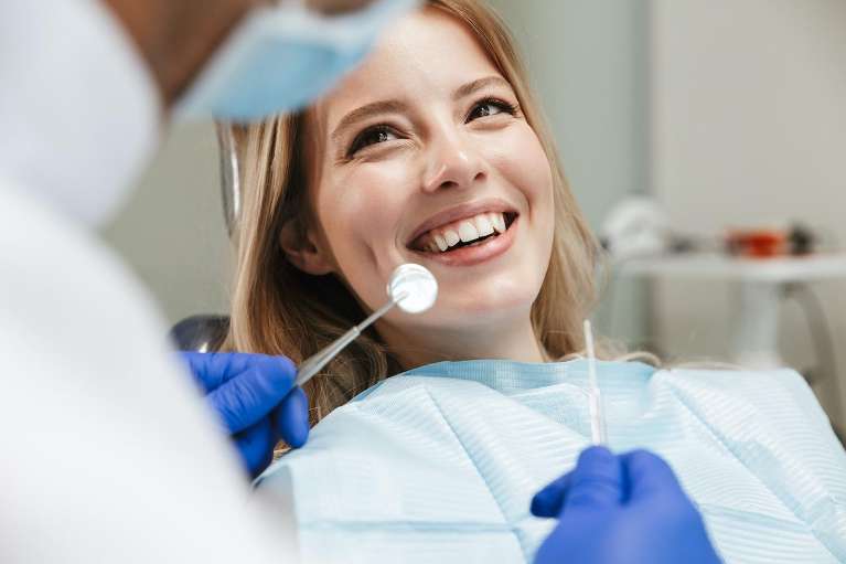 A woman smiles while seated in a dentist chair, ready for a dental crown procedure.