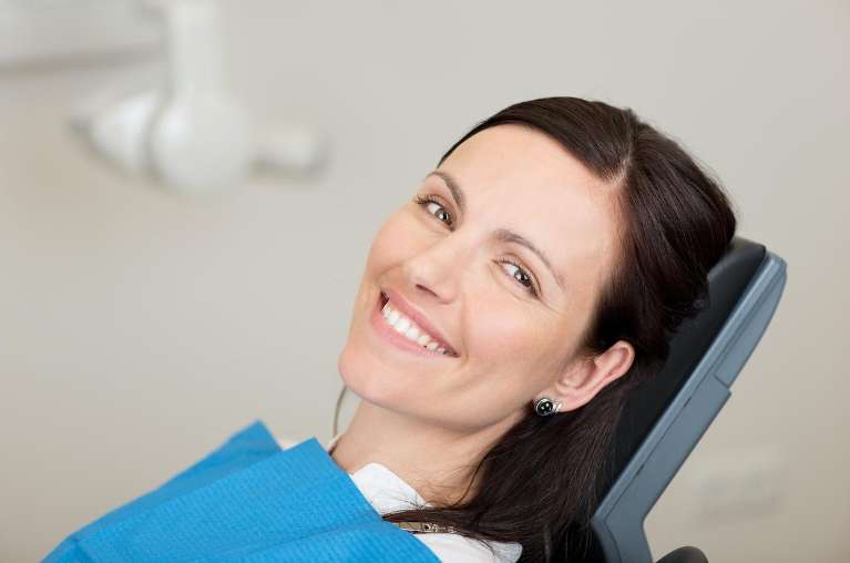 A smiling woman sits comfortably in a dental chair, ready for her dental crown procedure