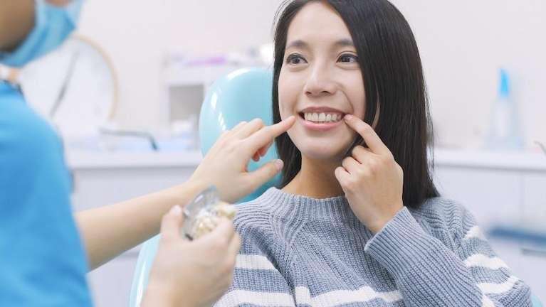 Asian woman pointing to her teeth in dentist chair, foothill ranch ca