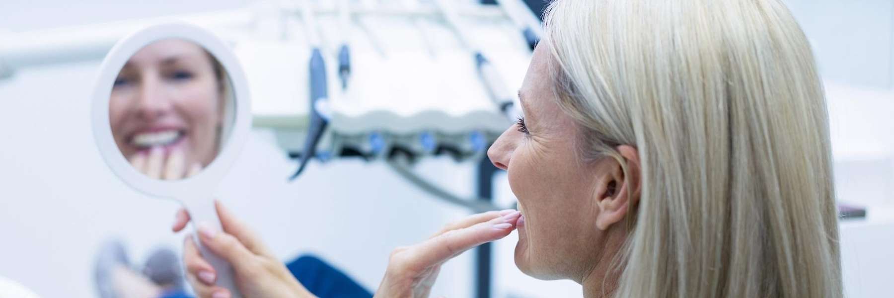Smiling woman checking her teeth in dental mirror highlighting solutions for struggling with loose p