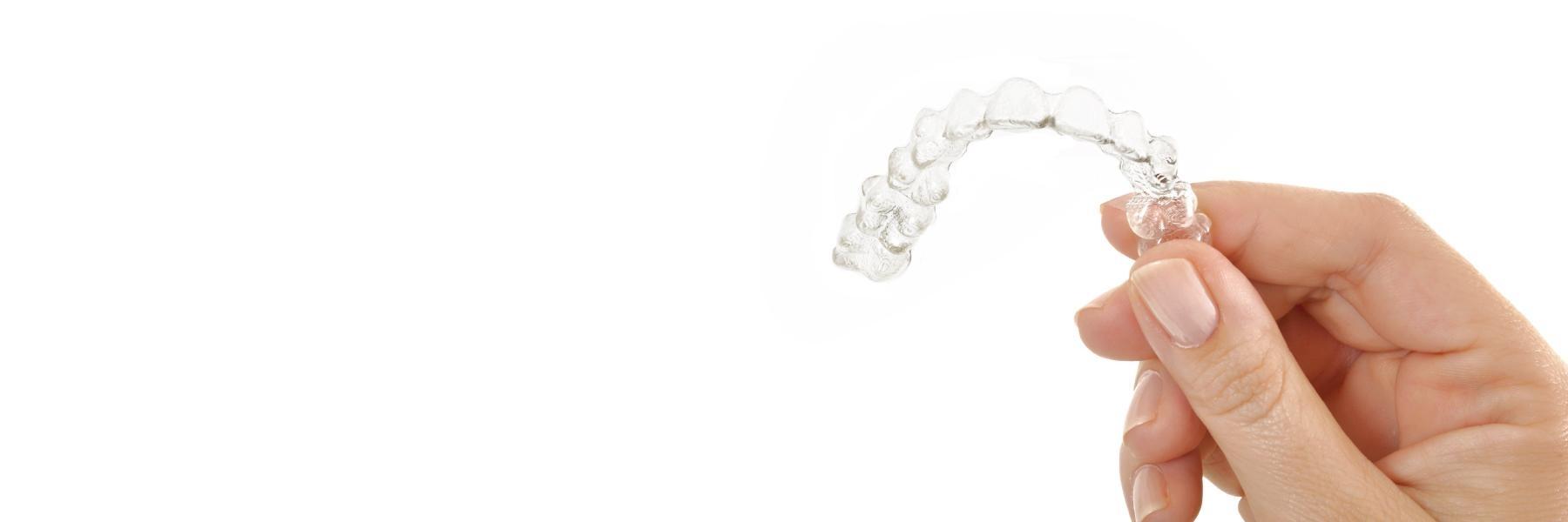 Hand holding Invisalign aligner at dentist near me Foothill Ranch